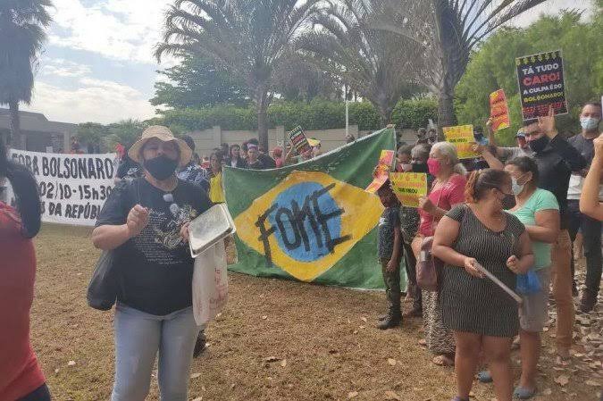 Com cartazes e palavras de ordem contra a fome e contra o aumento no preço dos alimentos, grupo está em um gramado na entrada do condomínio Mansões Dom Bosco